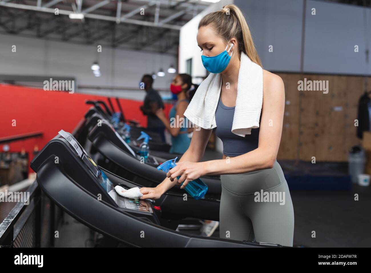 Fit caucasian woman wearing face mask sanitizing cardio machine before working out in the gym Stock Photo