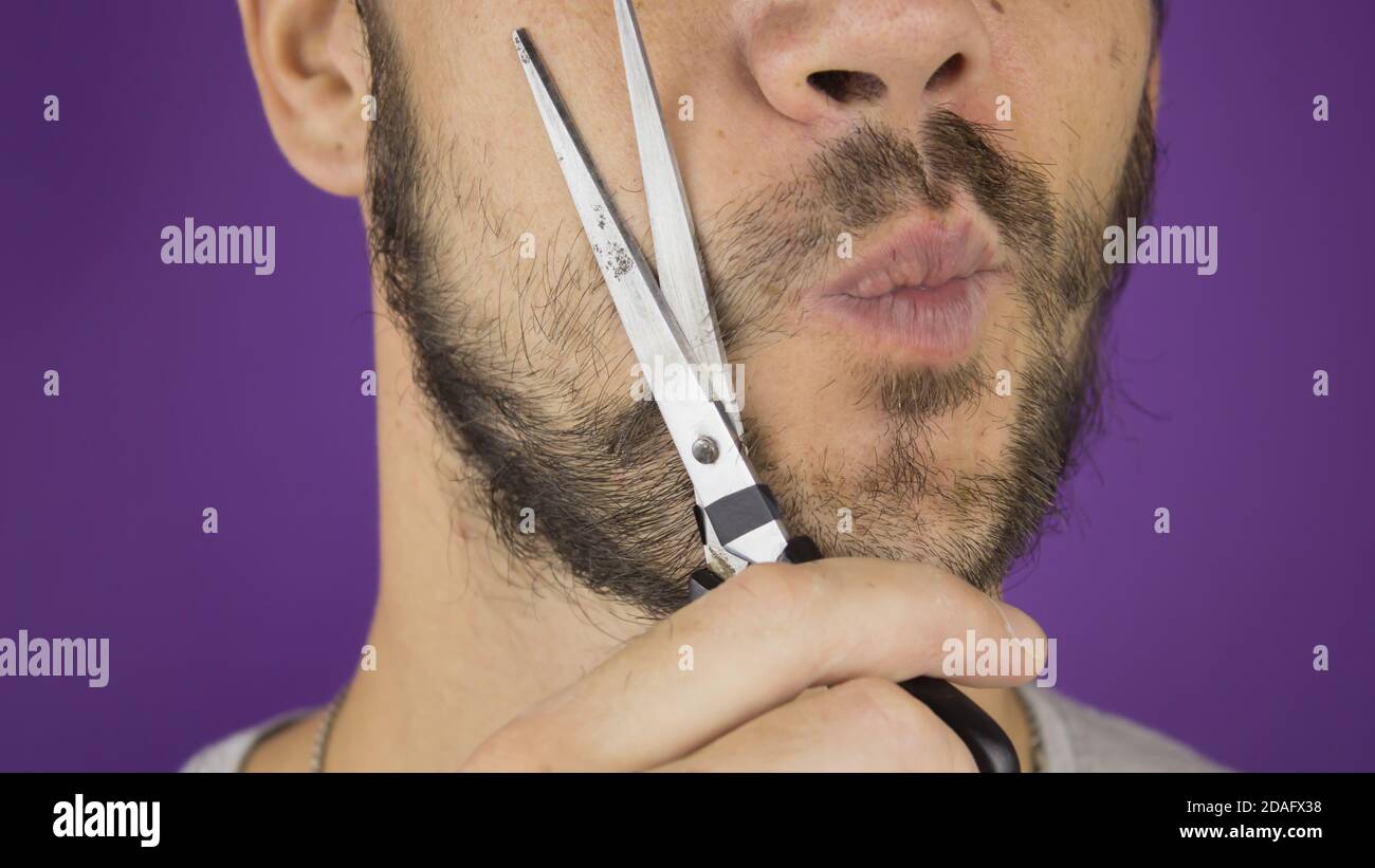 Handsome young guy trims his beard with scissors. Stock Photo
