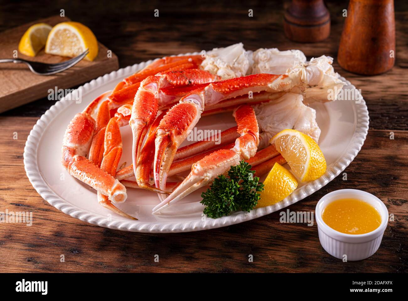 A plate of delicious snow crab leg clusters with lemon, parsley and melted butter. Stock Photo