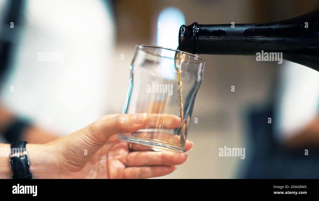 Close up and selective focus view hand holding a glass and bottle pouring white wine to taste, winery tasting. Stock Photo