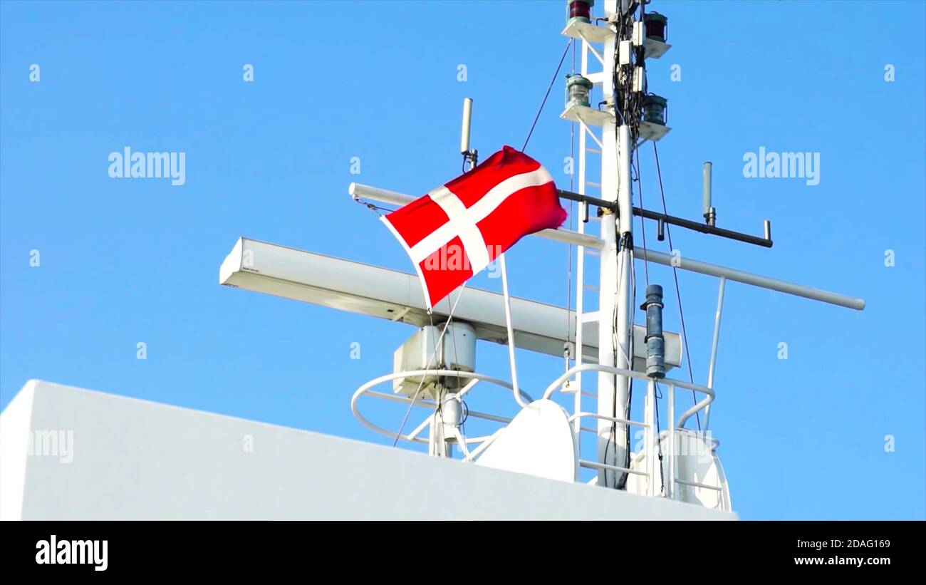 Danish flag on modern ship next to navigation and antenna and radar equipment against blue sky. Stock Photo