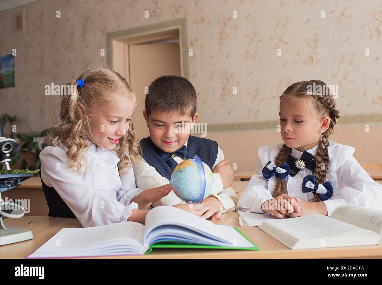two girls and a boy at school at a Desk studying geography watching the ...