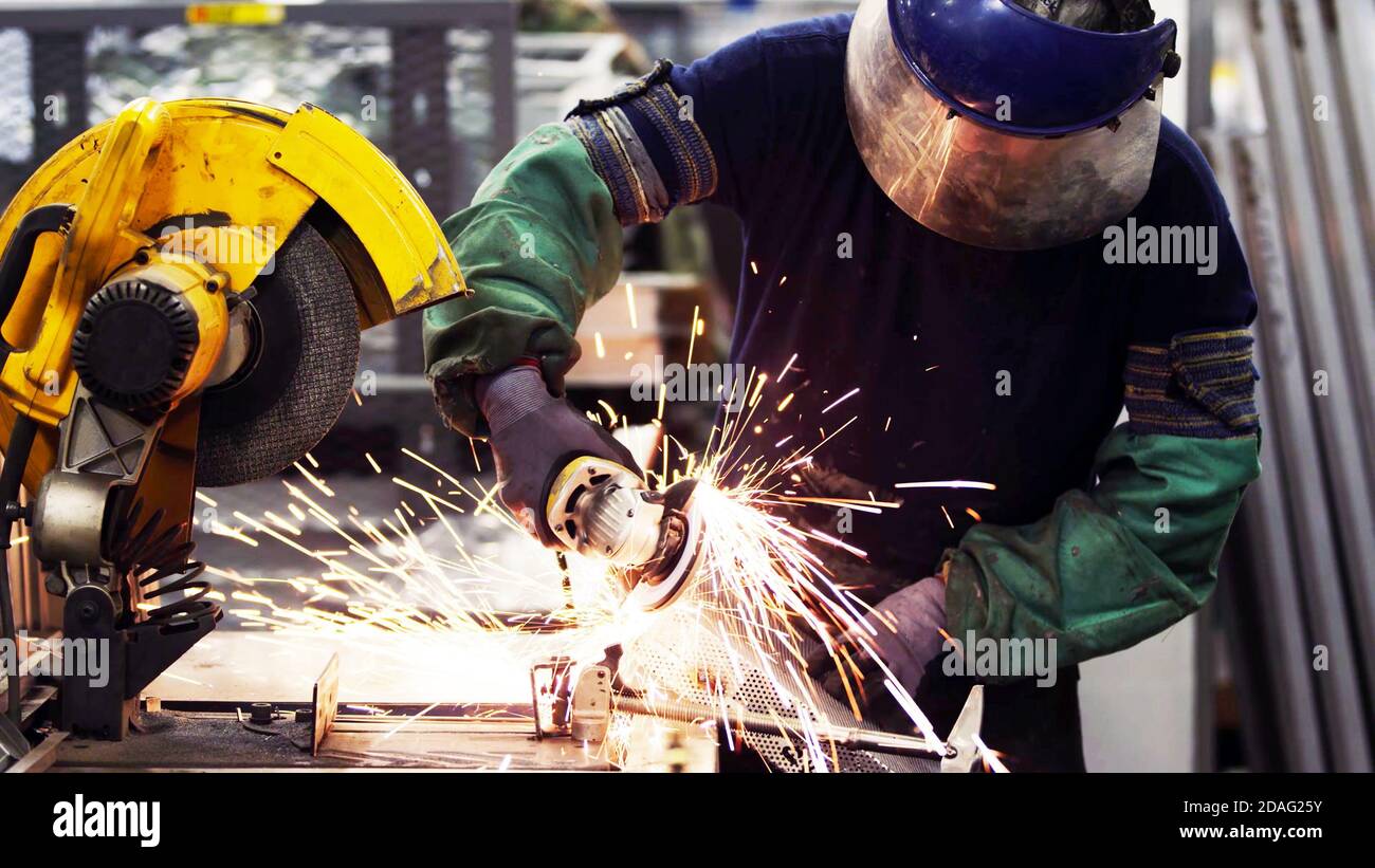 Heavy industry worker cutting steel with grinder machine in industrial manufacture, wearing safety equipments Stock Photo