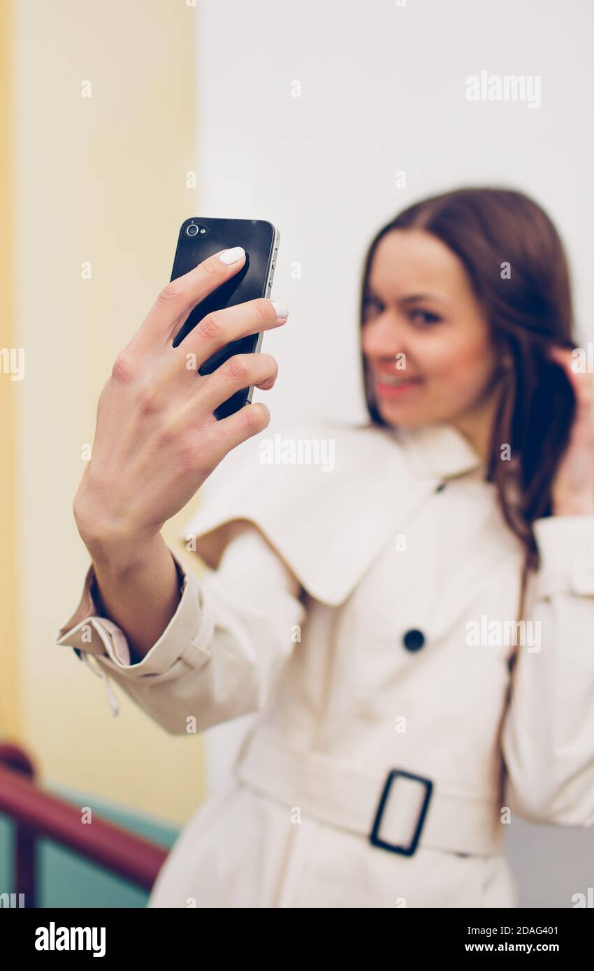beautiful young girl in a light raincoat takes a selfie on her phone ...