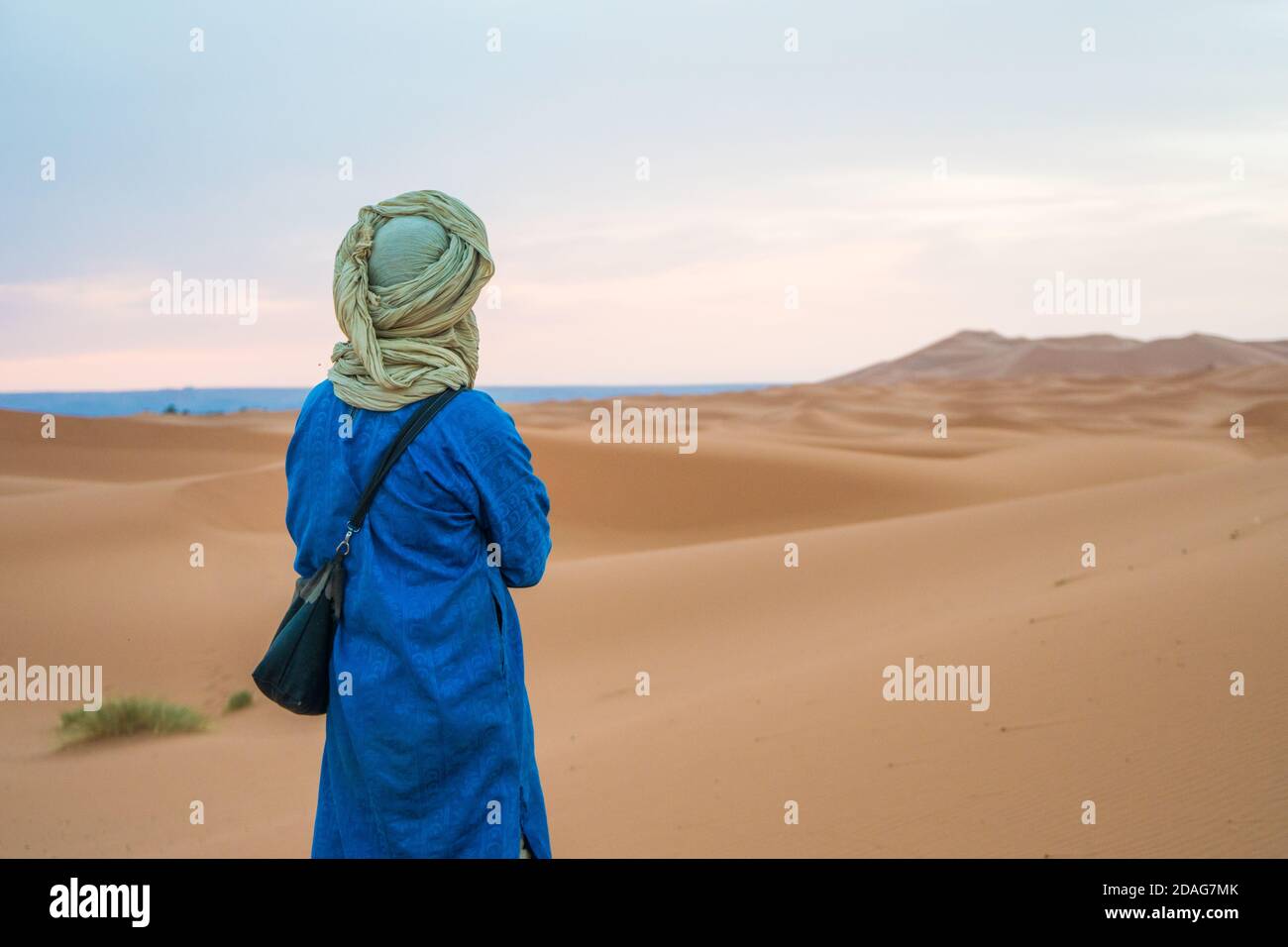 Merzouga, Morocco - APRIL 29 2019: Traditionally dressed Moroccan standing with the back to the camera and watching the Sahara Desert Stock Photo
