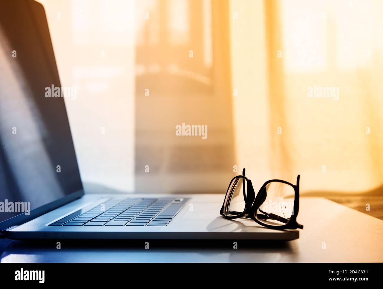 open laptop on which lie reading glasses in black frames. Stock Photo