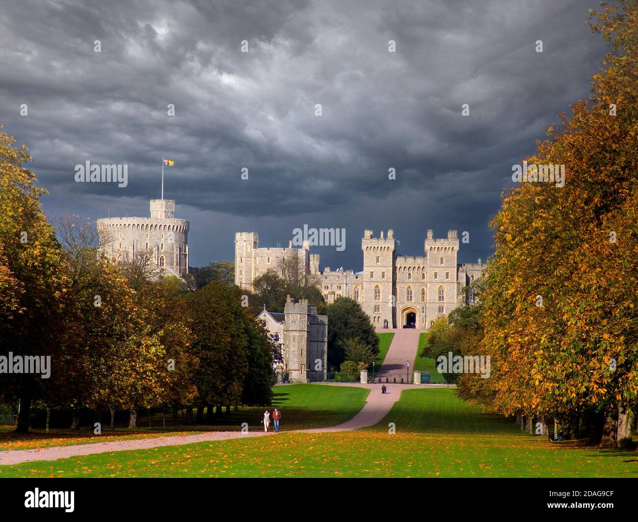 Windsor Castle & dark sky, flying Royal Standard with HM Queen Elizabeth  in residence, viewed down the Long Walk with walkers, in autumnal colour with dramatic shafts of sunlight and dark brooding stormy sky Windsor Berkshire UK Stock Photo