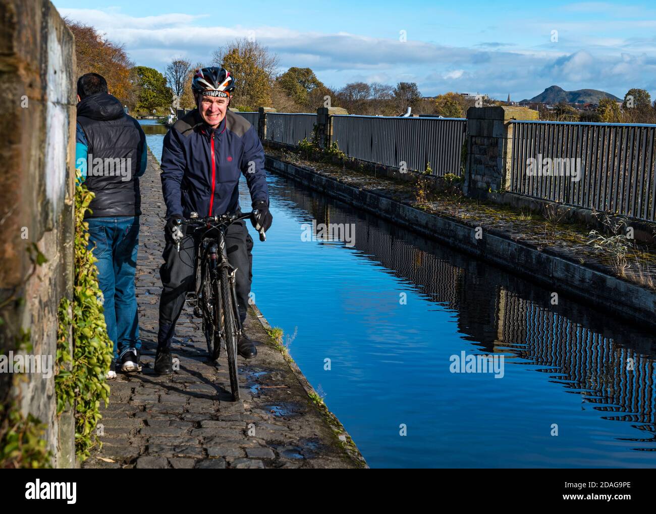 Man cycling across narrow towpath on Slateford Aqueduct into the path of a walker or pedestrian during pandemic, Union Canal, Edinburgh, Scotland, UK Stock Photo