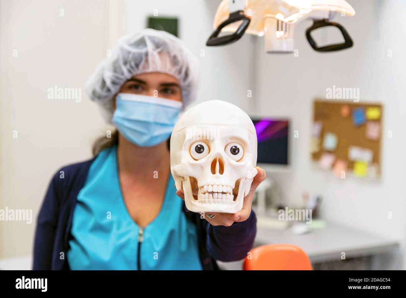 A doctor in medical uniform, hygiene headcover and face mask holding skull in hand Stock Photo