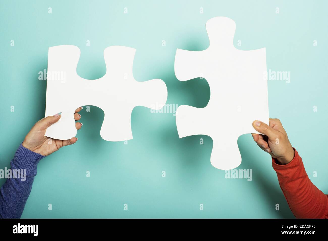 Two peoples join piace of puzzle. Concept teamwork, partnership, integration. Cyan background Stock Photo