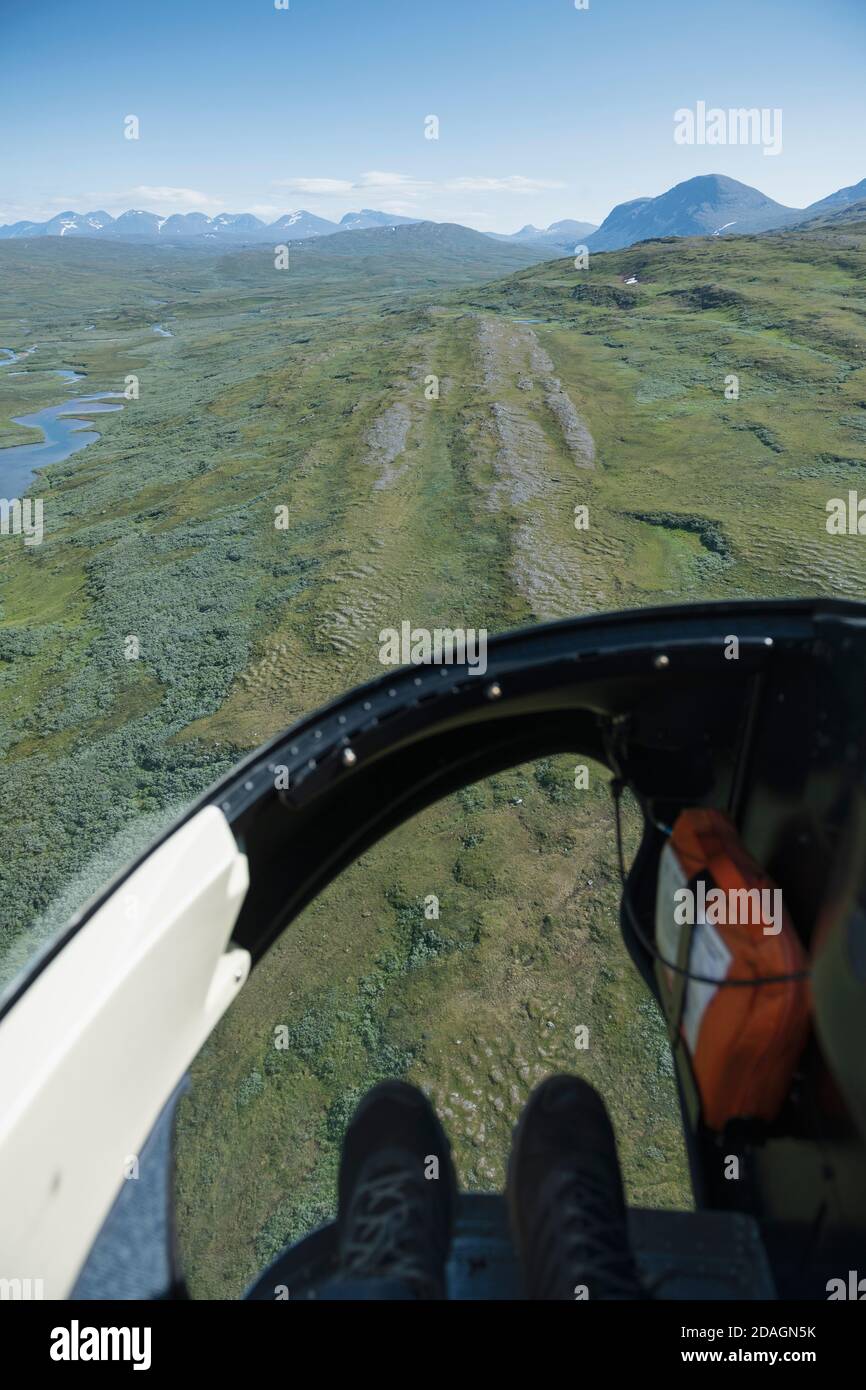 Feet in helicopter airtaxi flying over Padjelantaleden Trail towards Kvikkjokk, Lapland, Sweden Stock Photo
