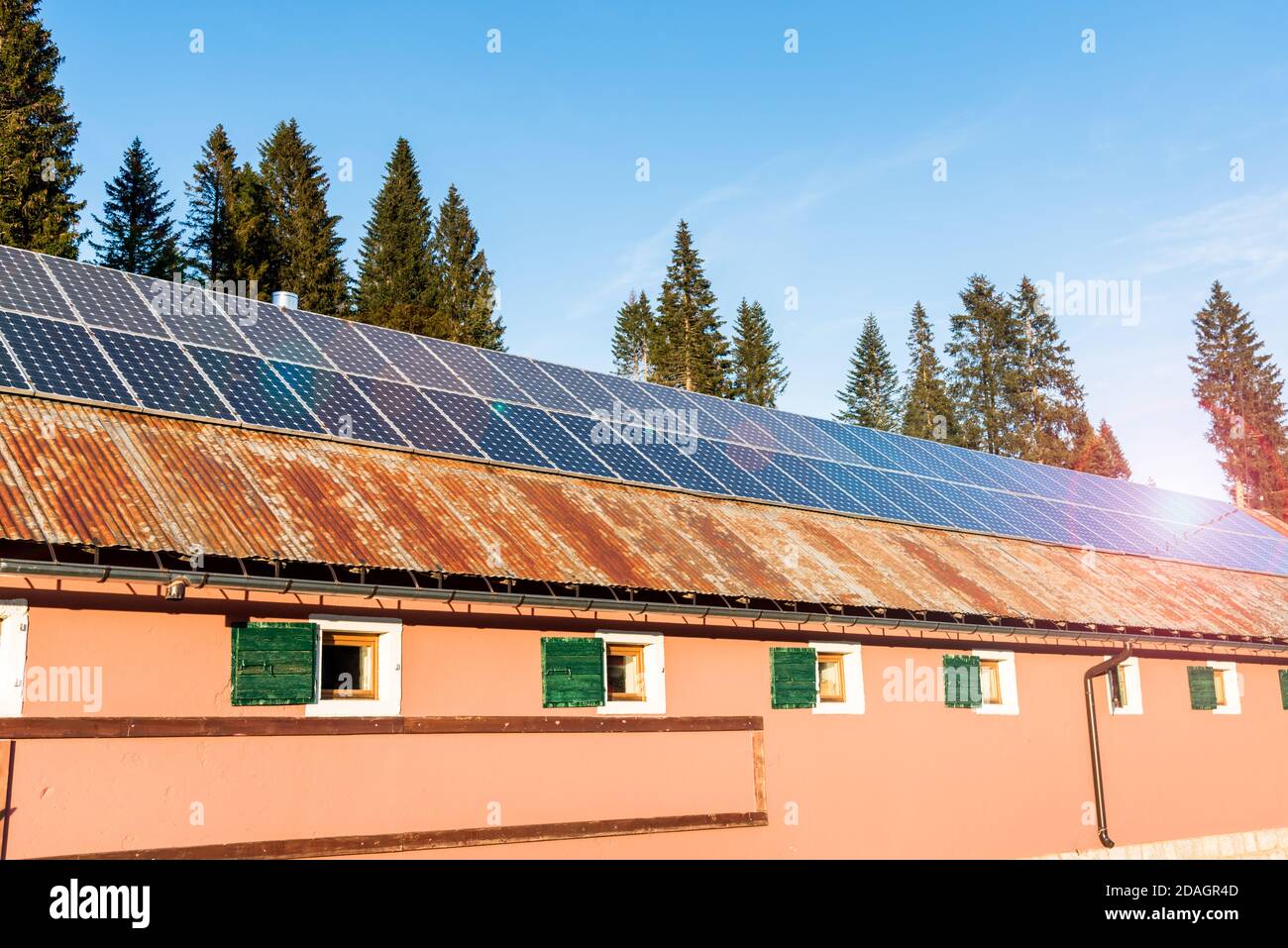 Solar panels for electricity generation over the rusty tin roof of a barn in the European Alps on a sunny autumn day. Lens flare. Stock Photo