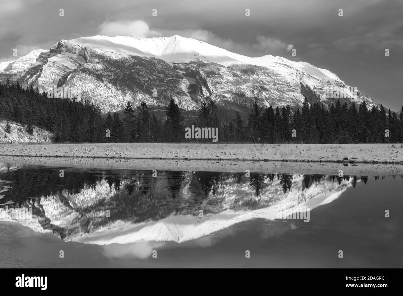 Monochrome or Black and White Landscape Image of Snowy Mountain Peak reflected in Calm and Cold Lake Water above Canmore, Alberta, Canadian Rockies Stock Photo