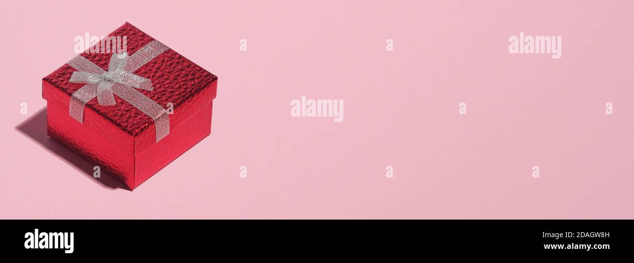 Red gift box with white ribbon bow on pastel pink background with copy ...