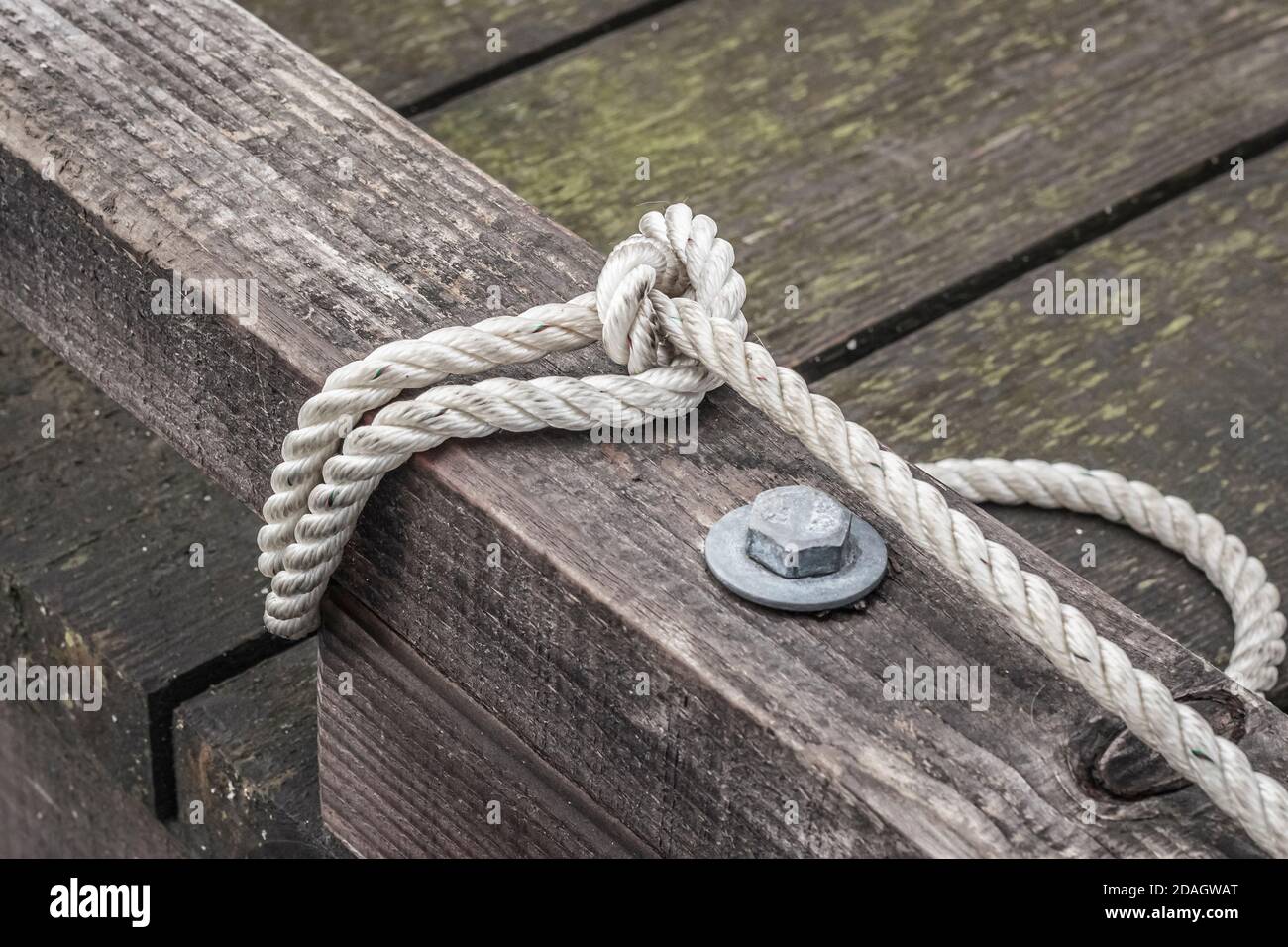 A white three-strand rope, securing a boat, is looped around a bull rail of a brown, weathered wooden dock on Canada's west coast (boat not visible). Stock Photo
