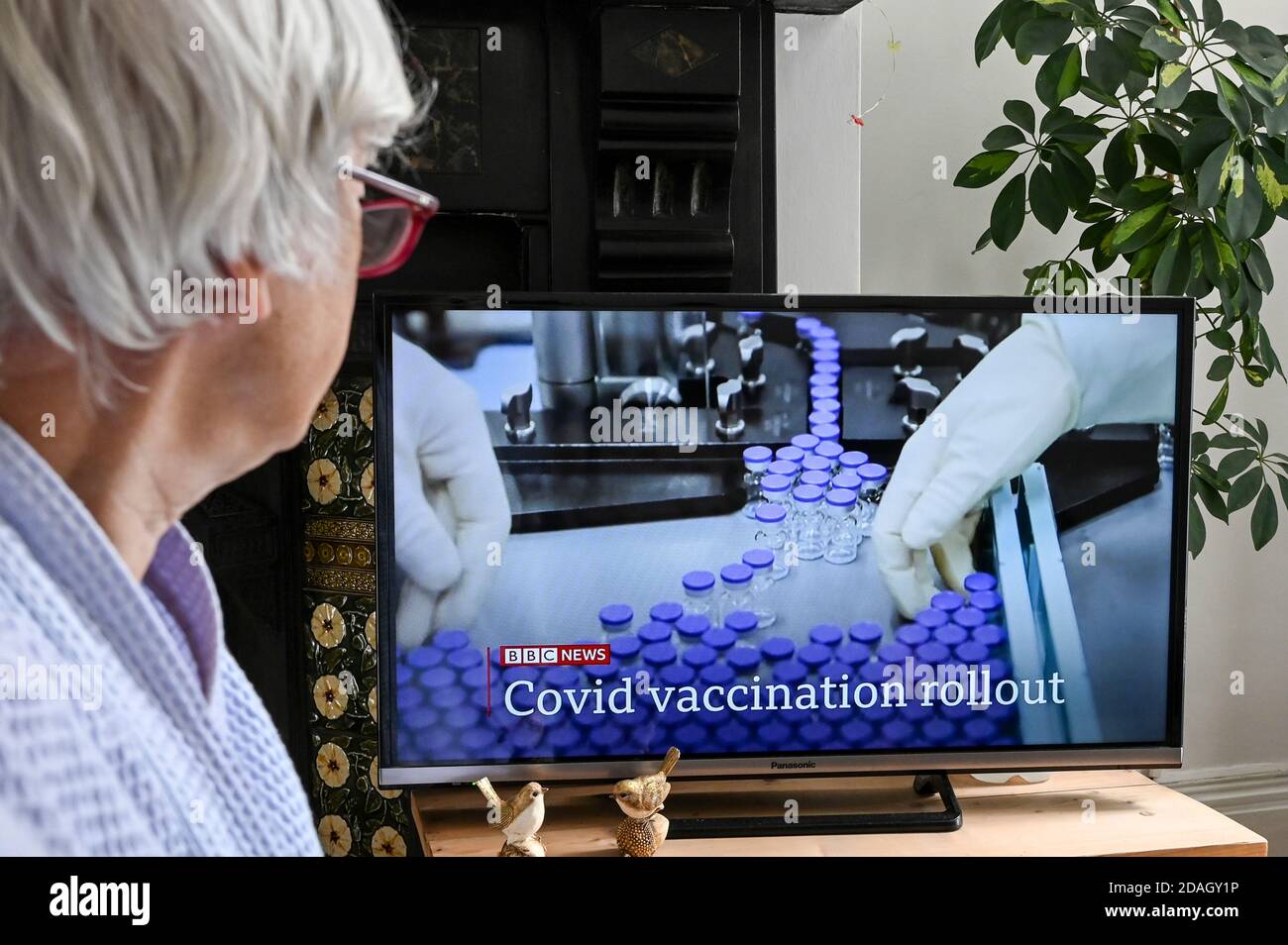 Televised announcement on BBC news of the new Coronavirus vaccine with caption 'Covid vaccination rollout' watched by a viewer. Stock Photo