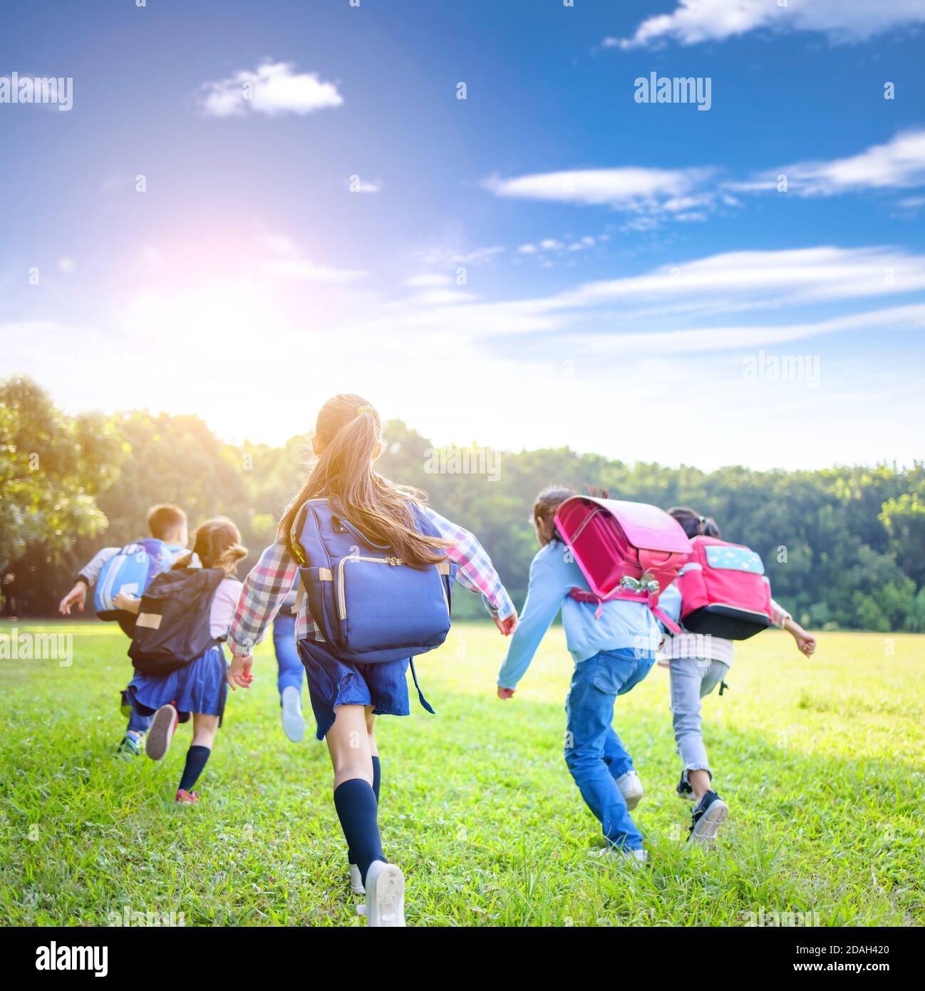 rear view of elementary school kids running on the grass Stock Photo
