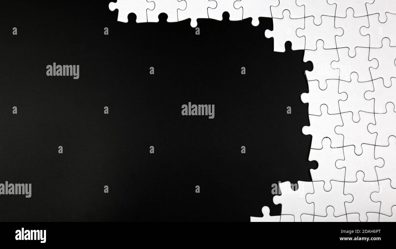 Unfinished white jigsaw puzzle pieces on black background Stock Photo
