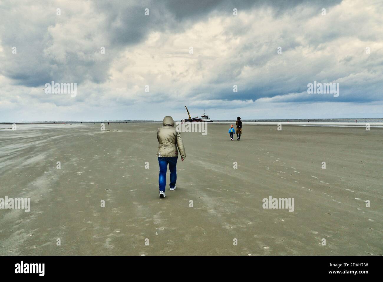 Epic clouds over beach with people walking in rear view. Extreme long shot. Stock Photo