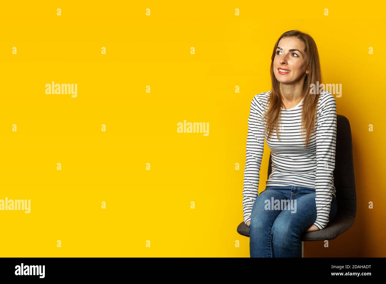 Young woman with a smile sits on a chair on a yellow background. Banner Stock Photo