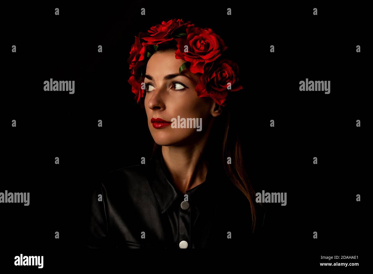 Pensive young woman in wreath of red flowers on black background. Stock Photo
