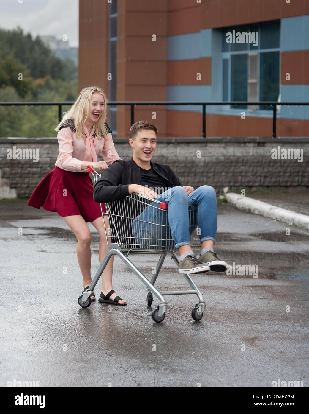 Young couple having fun on shopping trolley. Happy woman pushing ...