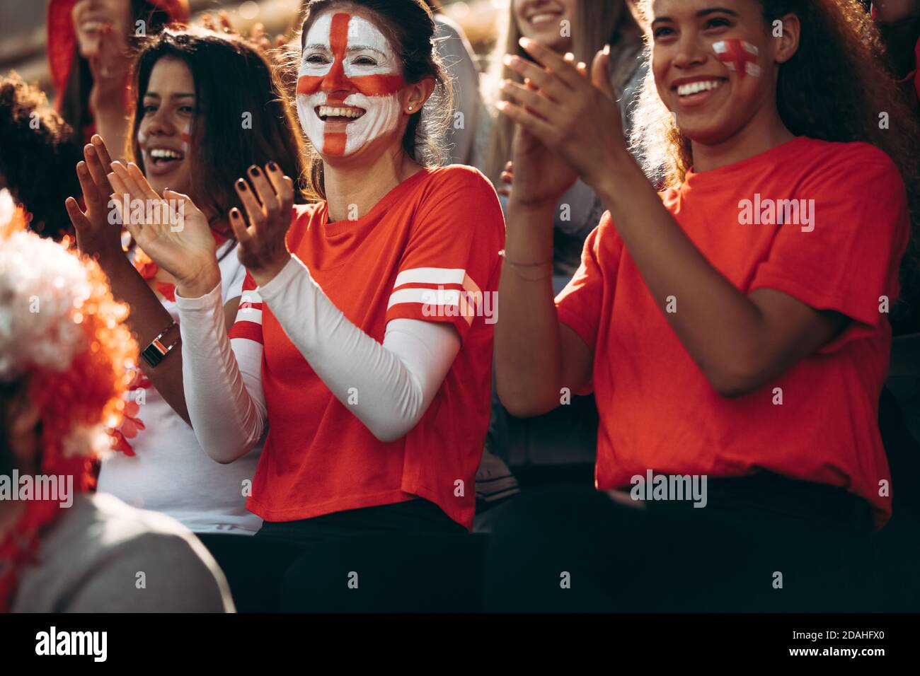 Happy young sports fans at live game clapping and cheering for their team. England football fans enjoying during a match. Stock Photo