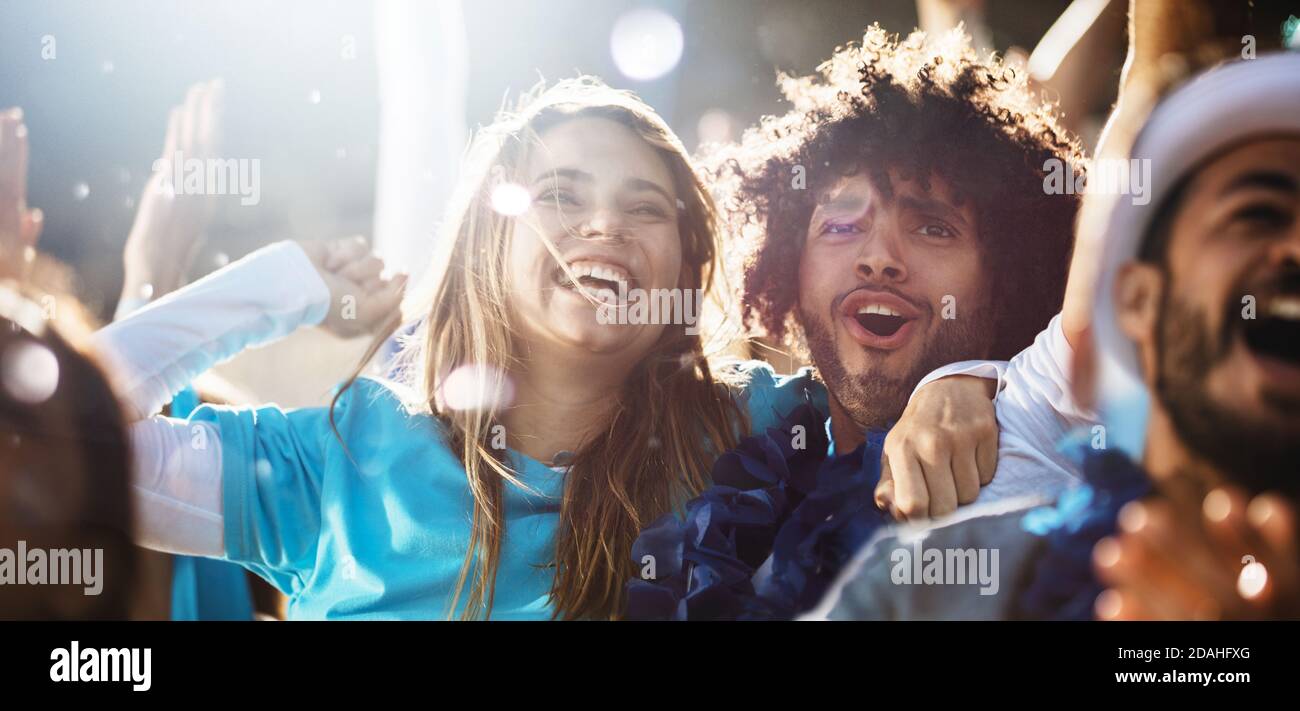 Cheerful couple cheering at a live soccer match. Group of people in the stadium cheering argentina football team. Stock Photo