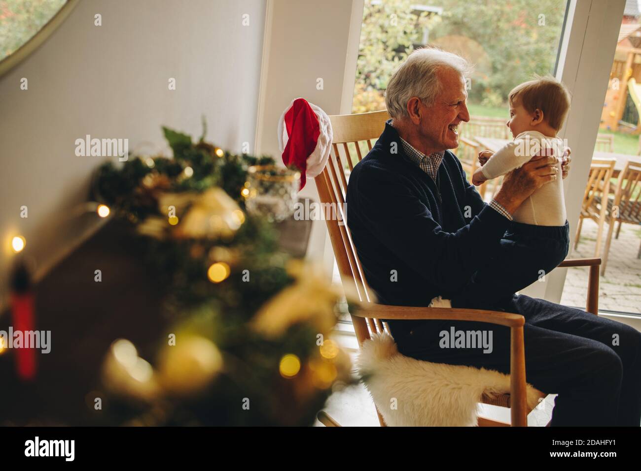 Elderly man with his grandson on a christmas eve. Grandfather holding his grandson sitting on chair. Stock Photo