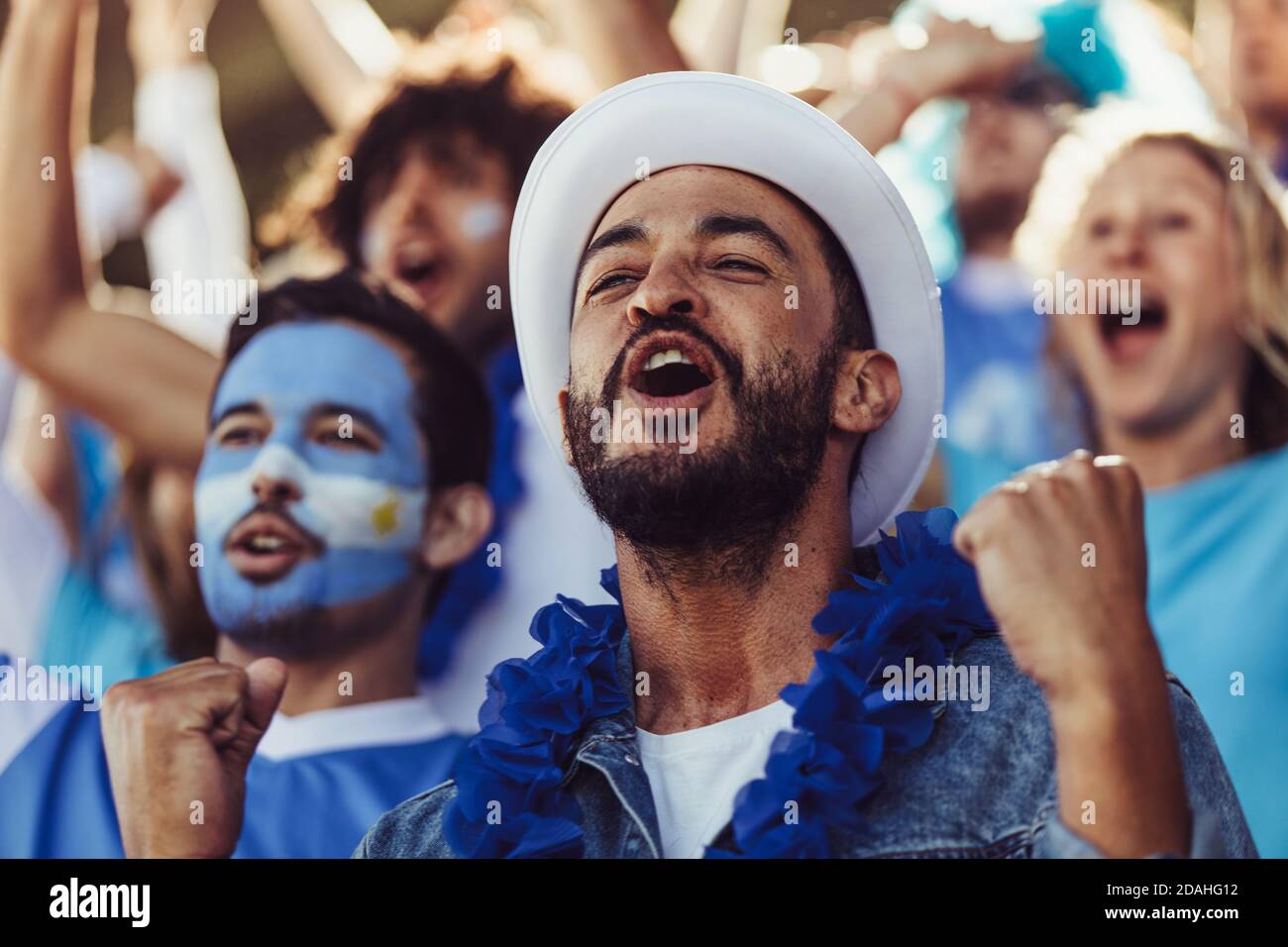 Crowd of soccer fans from Argentina cheering their team with a blue garlands and argentinian flags at stadium. Football fans sitting at stadium cheeri Stock Photo