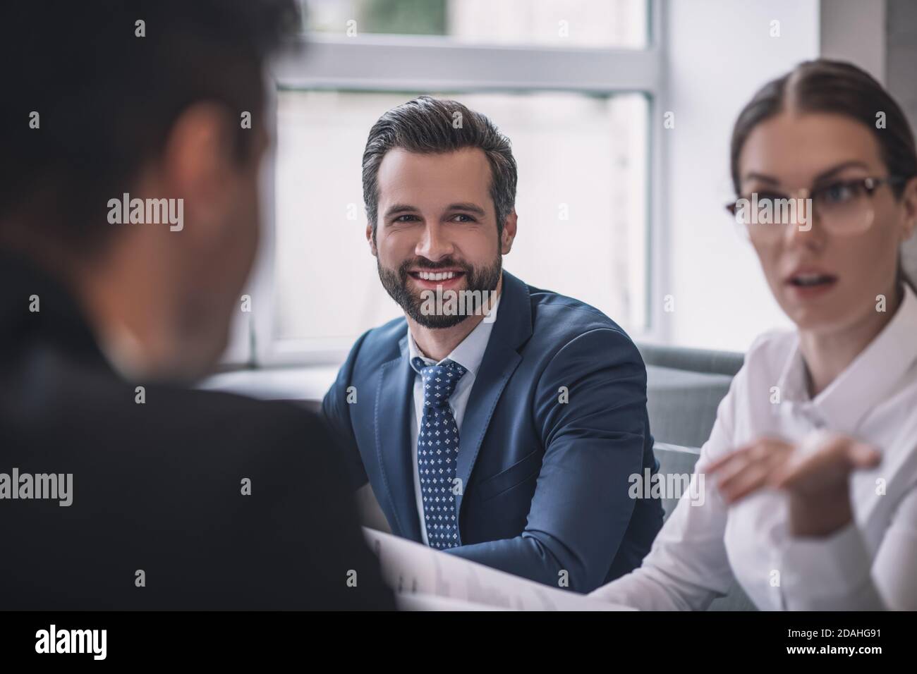 Gesturing serious woman, smiling man and colleague back Stock Photo
