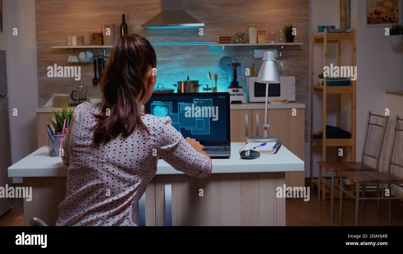 Woman scrolling programming security hacking code data late at night on laptop. Programmer writing a dangerous malware for cyber attacks using performance device during midnight. Stock Photo