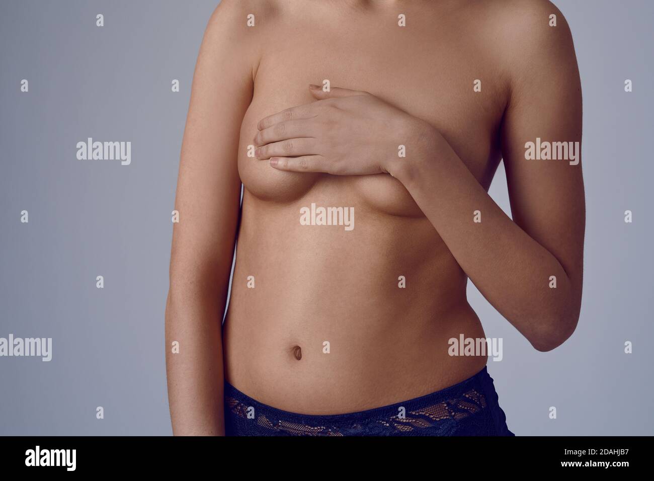 Close-up on topless woman pressing her breast, pressing with one hand. Check for breast cancer concept. Cropped impersonal portrait in studio, against Stock Photo