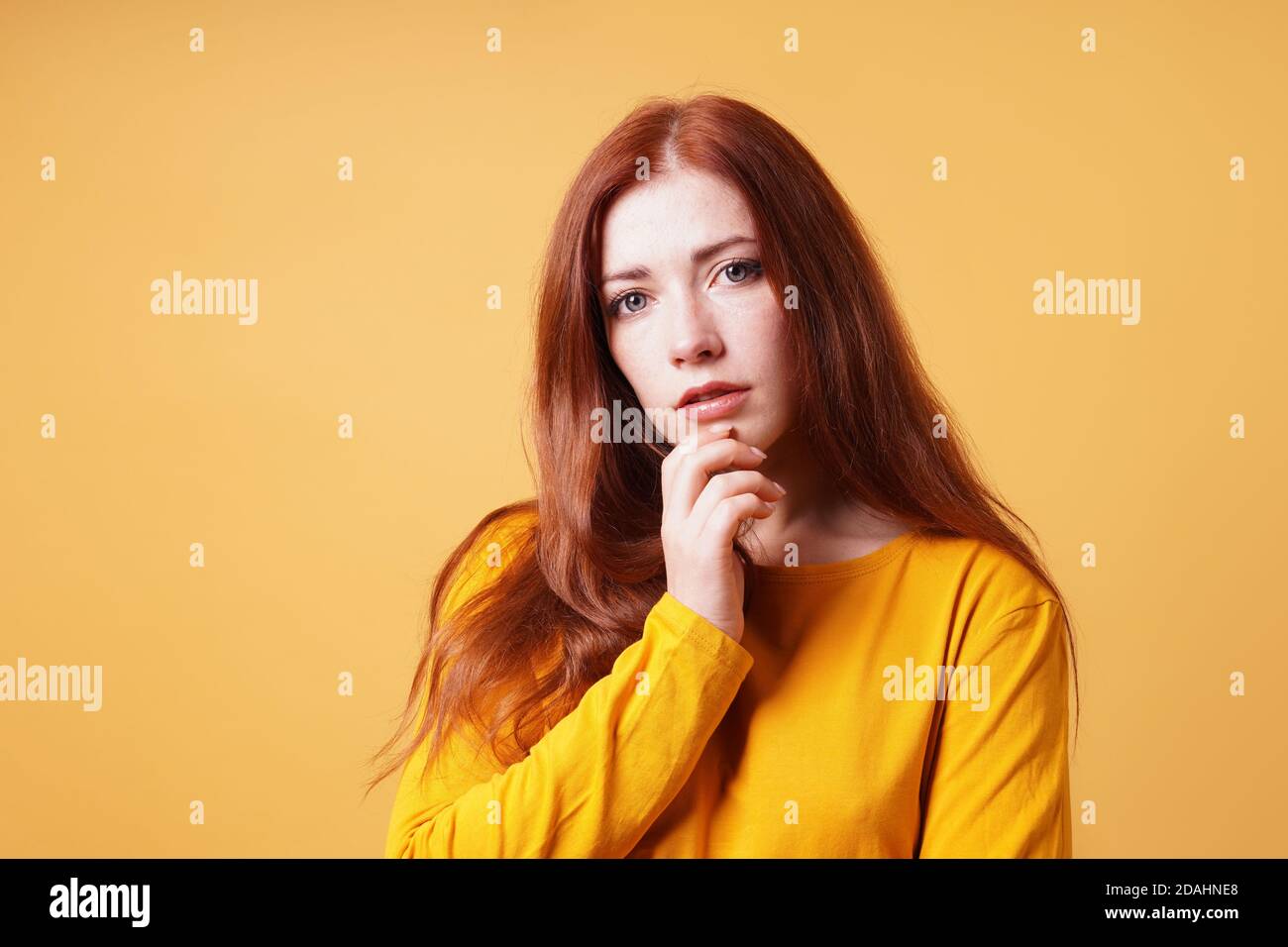 thoughtful young woman with finger on chin gesture - yellow orange color background with copy space Stock Photo