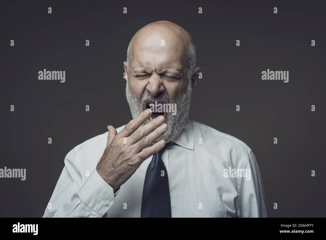 Lazy tired middle-aged businessman yawning and feeling sleepy, he is covering his mouth with his hand Stock Photo