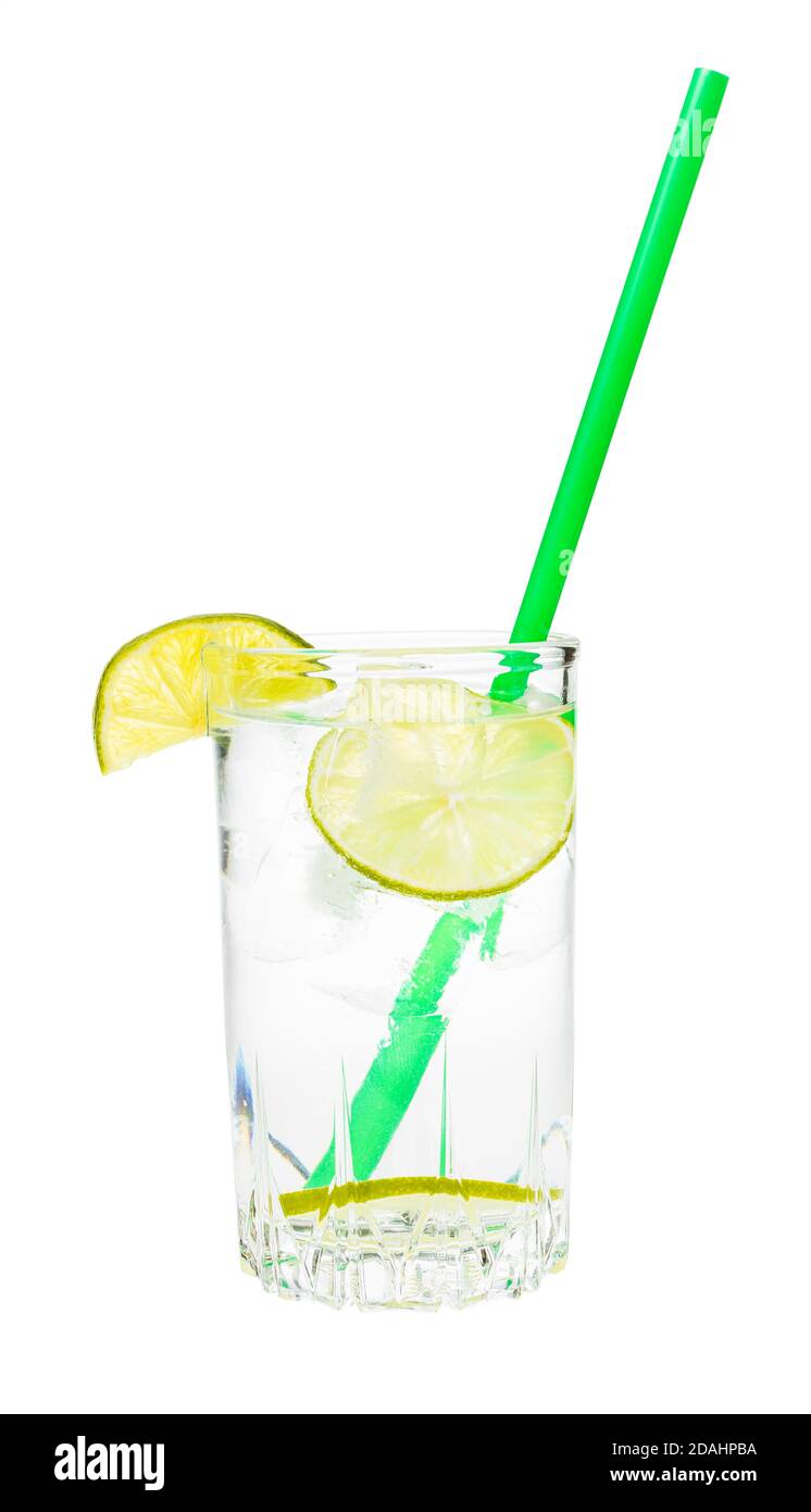 side view of glass with prepared gin and tonic cocktail on the rock with wedge and slices of lime and green plastic straw isolated on white background Stock Photo