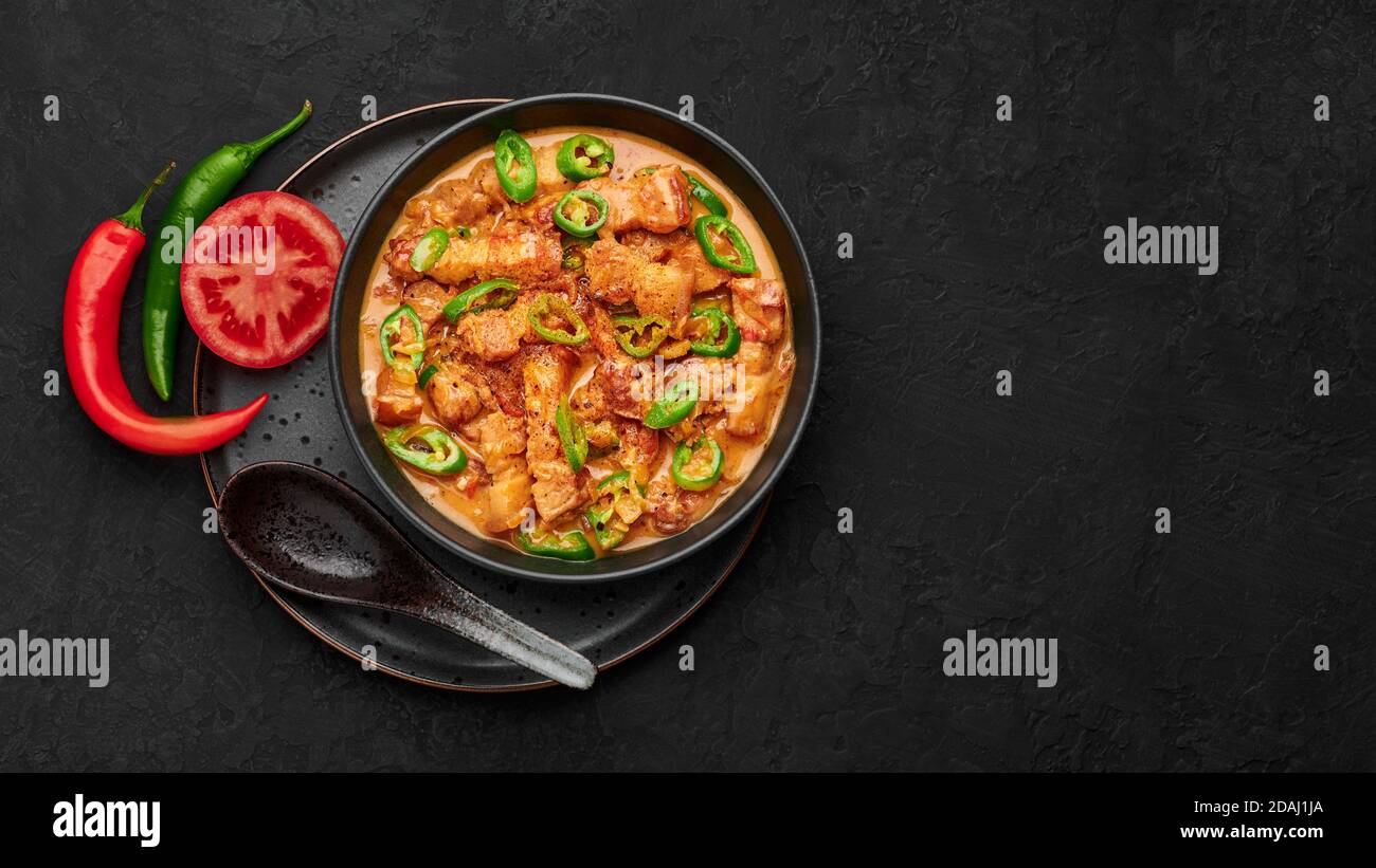 Bicol Express Stew in black bowl on dark slate table top. Filipino cuisine spicy pork belly
