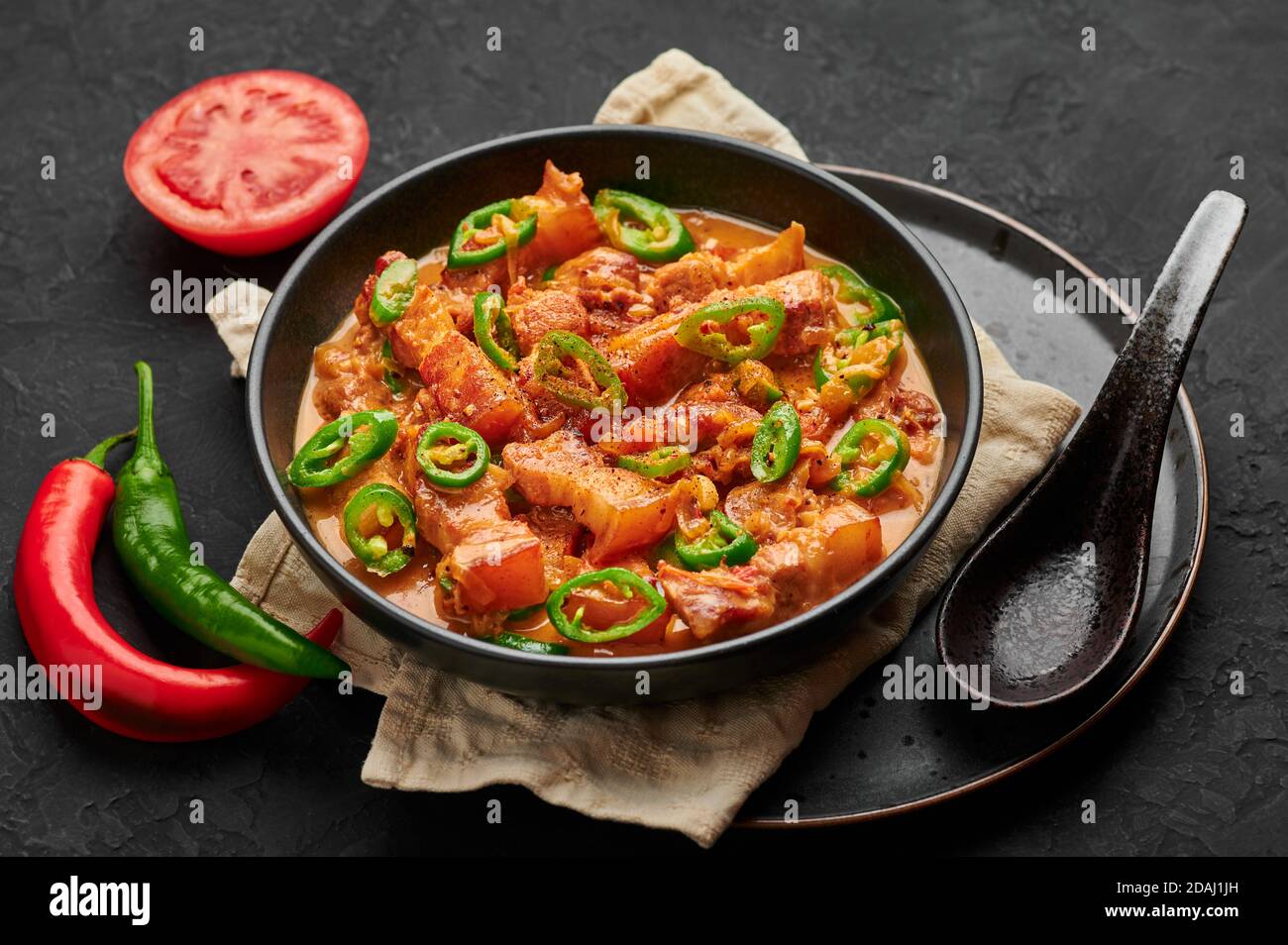Bicol Express Stew in black bowl on dark slate table top. Filipino cuisine spicy pork belly