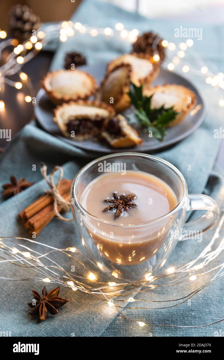 masala tea and sweet mince pies on a table with Christmas decoration. Masala chai is an Indian tea beverage made by boiling black tea in milk and water with a mixture of aromatic herbs and spices Stock Photo