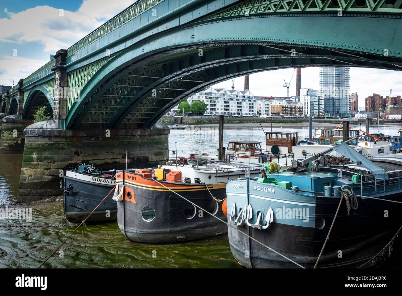 Barges converted into house boats, sit on the River Thames mud at low tide under Battersea Railway Bridge (originally called the Cremorne Bridge Stock Photo