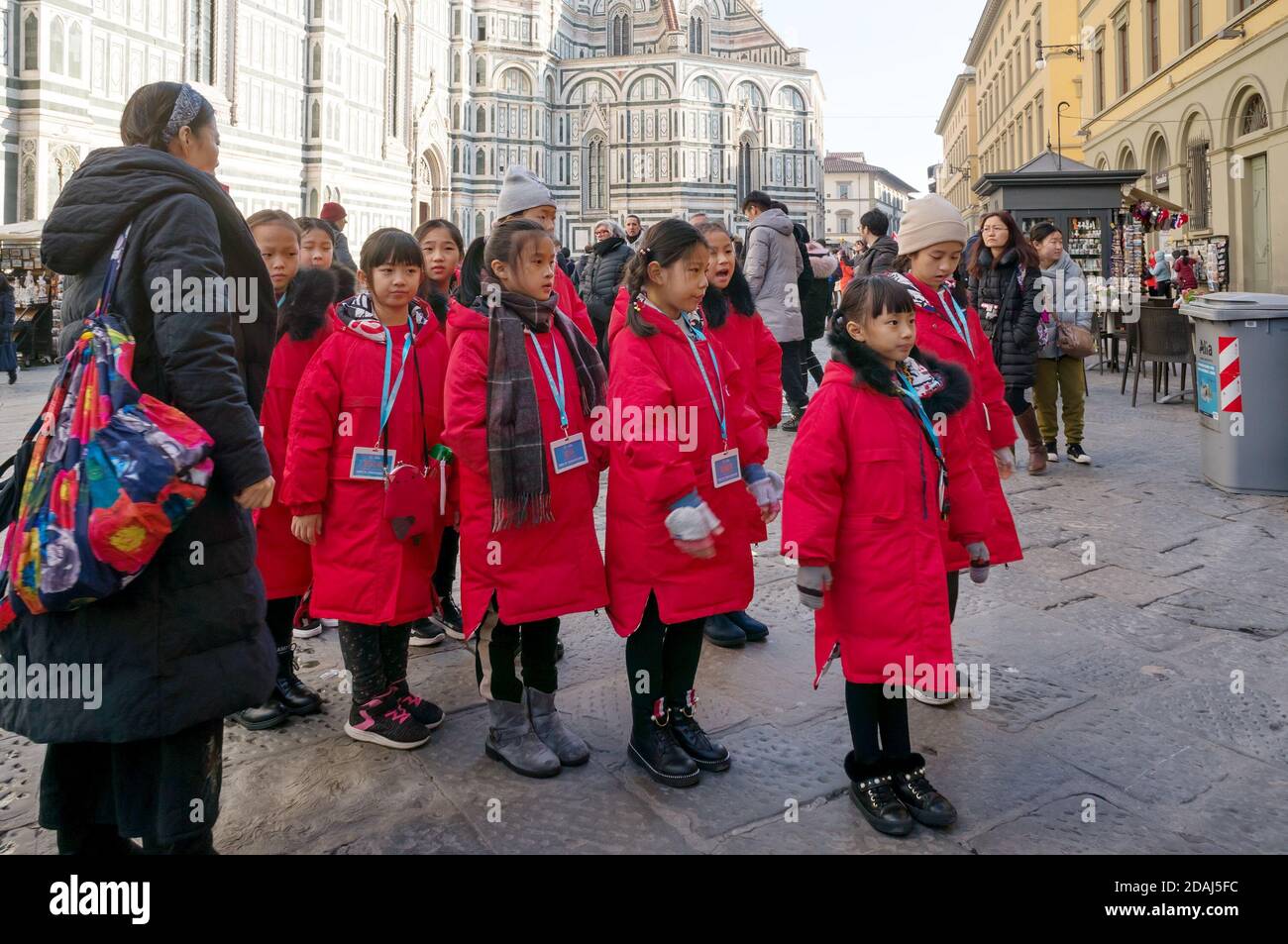 Tour group of Asian girls stands near Medieval religious building of the baptistery of San Giovanni. Florence, Italy. Stock Photo