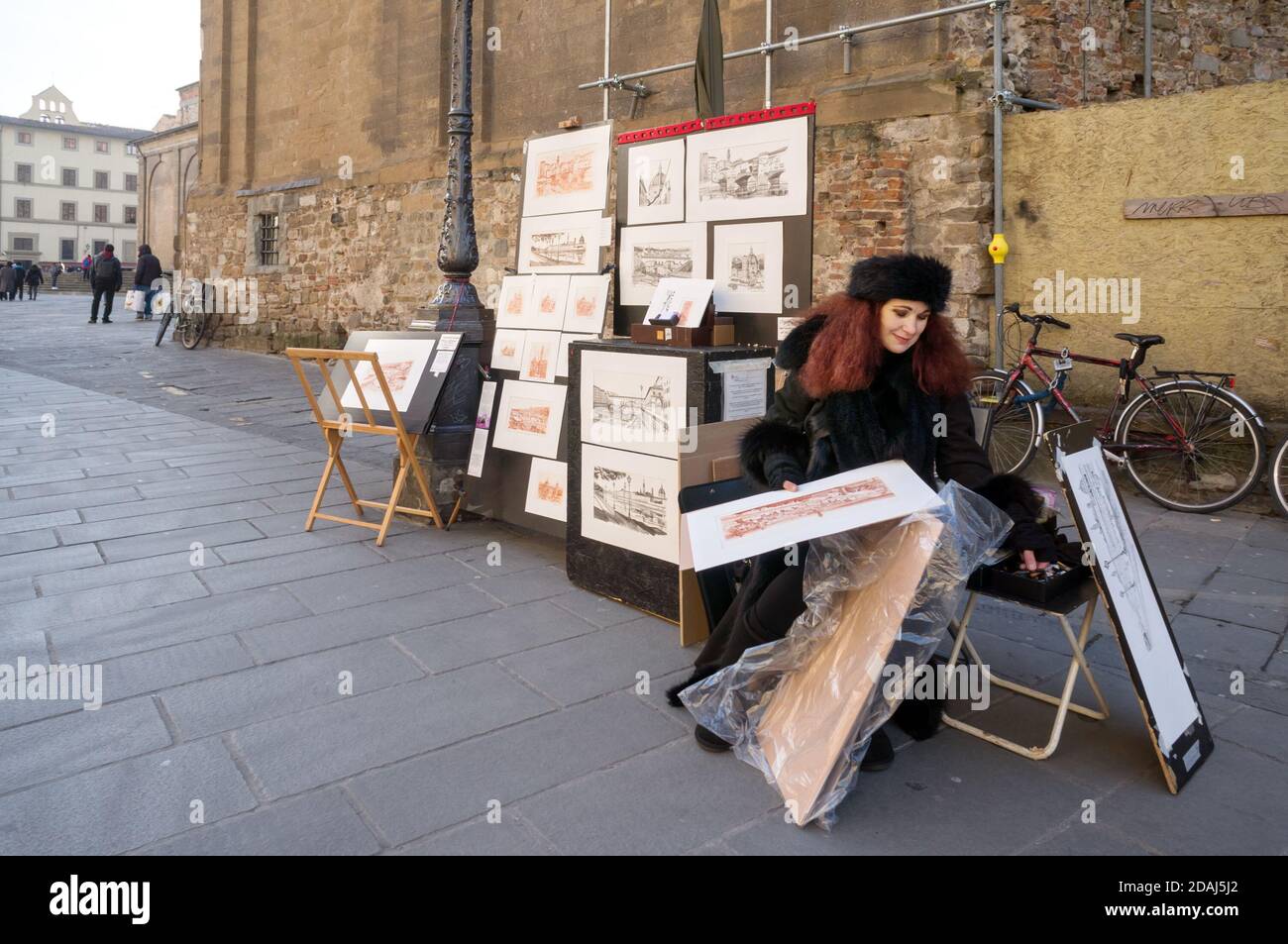 A female artist sells her paintings near the wall of a building in a