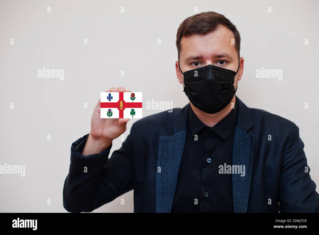 Man wear black formal and protect face mask, hold Montreal flag card isolated on white background. Canada cities coronavirus Covid concept. Stock Photo