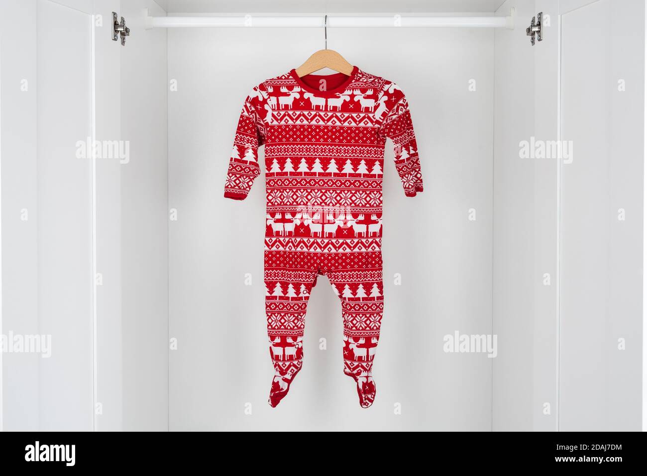 Horizontal color image with a front view of a white and red christmas pajamas hanging on a wooden hanger in the middle of a white closet. Stock Photo