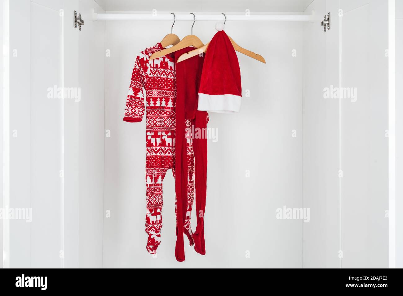 Horizontal color image with a front view of a white and red christmas pajamas, hat and tights hanging on a wooden hangers in the middle of a white clo Stock Photo