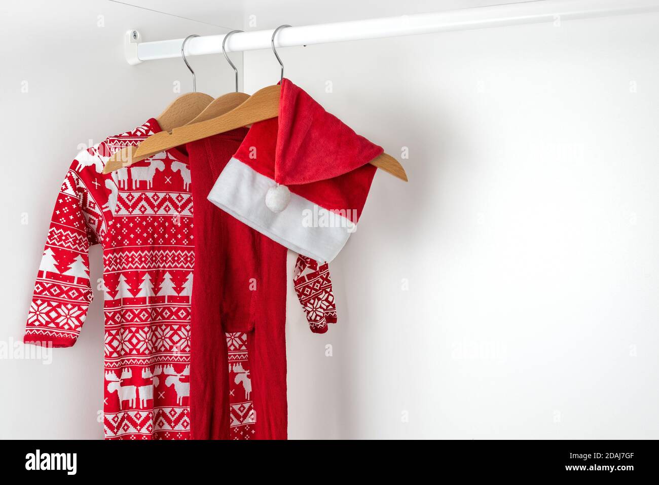 Horizontal color image with a side view of a white and red christmas pajamas, hat and tights hanging on a wooden hangers on the left of a white closet Stock Photo