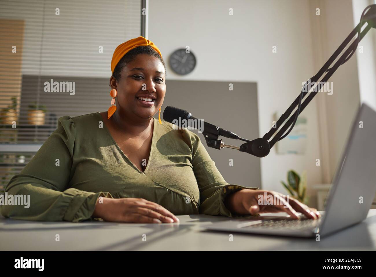 Portrait of African happy woman smiling at camera while sitting at the table with laptop and leading live broadcast Stock Photo