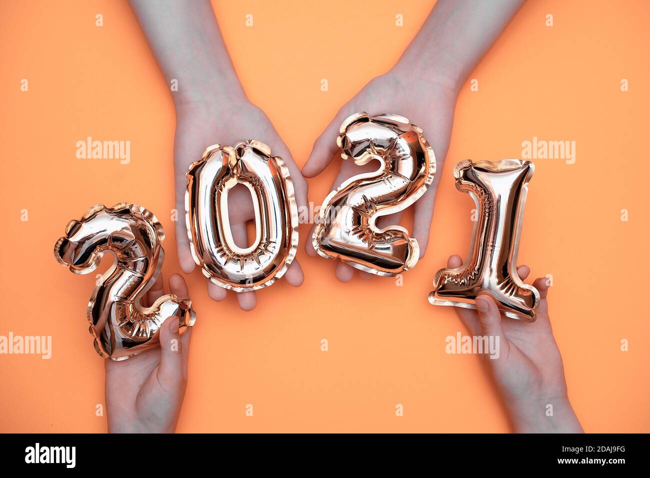 Golden new year numbers-balls 2021 held by people at arm's length up on a yellow background.  Stock Photo