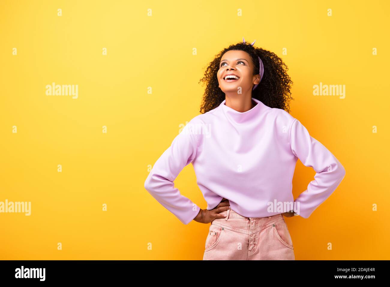 happy african american woman standing with hands on hips on yellow ...