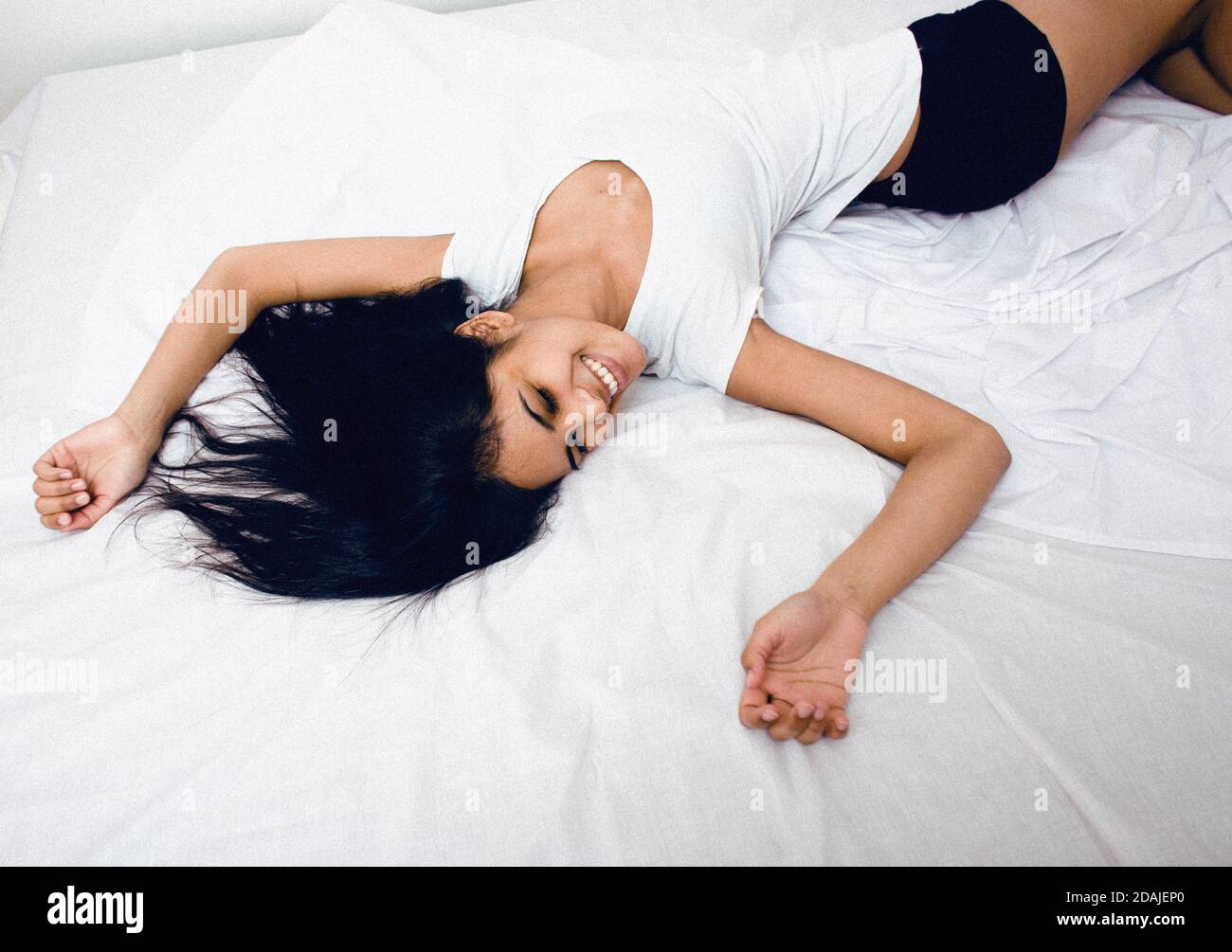 pretty indian brunette real woman in bed smiling, white sheets, tann skin close up . cant sleep Stock Photo